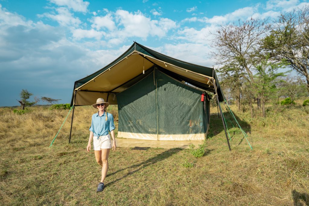 Safari outfit for women around camp: khaki shorts, light blue long sleeve shirt, trail runners, and sun hat. What to wear on safari for women.